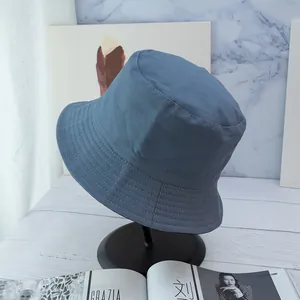 Detailed view of blue-gray cotton bucket hat stitching on a display stand with magazines