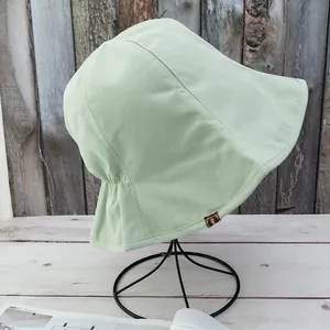 Close-up of light green cotton sun hat featuring a brown handmade label and ruched back