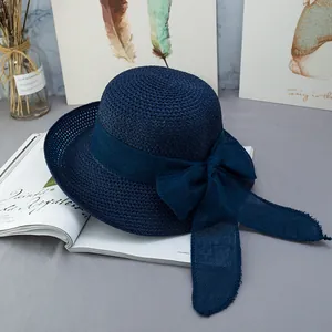 Dettaglio cappello di paglia blu navy a tesa larga con fiocco su sfondo rivista elegante