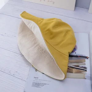 Close-up of yellow cotton bucket hat on a wooden table next to a magazine