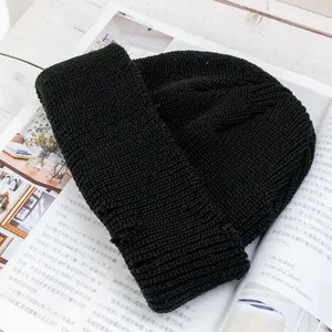 Detalle de un gorro de punto acanalado negro sobre una revista en un escritorio blanco