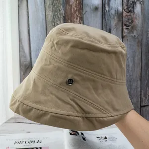 Detailed texture of khaki cotton bucket hat featuring a round black metal M badge