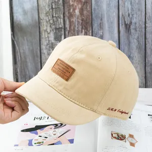 Détail de la casquette beige en coton avec écusson en cuir et broderie rouge latérale
