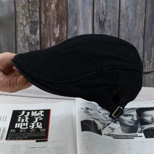 Detail of black cotton beret cap featuring bronze adjustable metal buckle and stitching