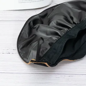 Close-up of a black sun hat with satin lining and elastic strap on a wooden surface