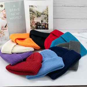 Solid knit beanie hats in multiple colors stacked on marble background for winter