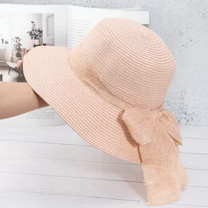 Détail d'un chapeau de paille rose avec large bord et grand nœud décoratif assorti