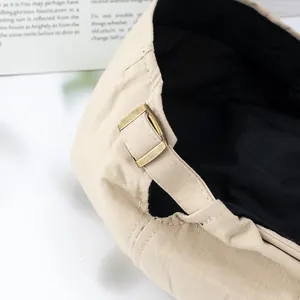 Detailed close-up of beige beret hat featuring an adjustable antique brass metal buckle