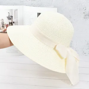 Détail d'un chapeau de paille beige tissé main avec un grand nœud et bord large