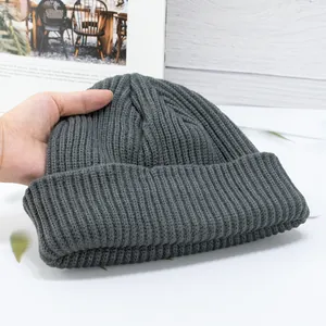Detailed view of dark grey thick ribbed knit beanie held by hand in home setting