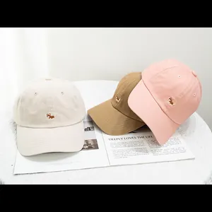 Detailed close-up of three cotton baseball caps with cute corgi dog embroidery in soft colors