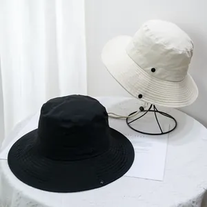 Detail of wide brim sun hats in black and beige with adjustable chin straps and metal buckles