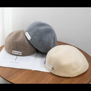 Detailed close-up of wool beret hats in brown, grey, and cream with silver metal labels