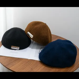 Three wool blend newsboy caps in black, navy and caramel placed on a wooden table