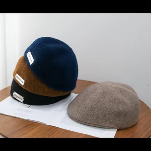 Detail of wool blend newsboy caps in navy, brown, and black stacked on a wooden desk