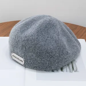Detailed texture of dark gray wool newsboy cap with silver metallic brand logo tag