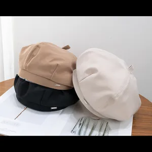 Trois bérets minimalistes en coton noir, kaki et beige sur une table en bois clair