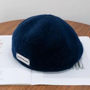 Detail of wool texture and silver metal logo plaque on a navy blue beret hat