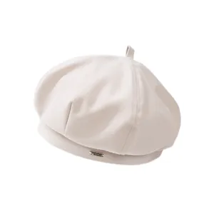 Détail du béret blanc cassé avec une plaque en métal argenté et un petit nœud sur le dessus