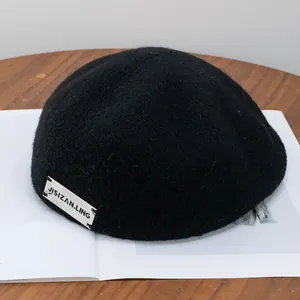 Detailed texture of black wool beret with a white minimalist woven letter label