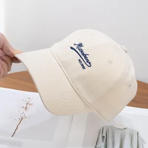 Close-up of beige cotton baseball cap featuring navy blue letter embroidery on the side