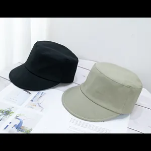 Flat top military caps in black and khaki canvas laid on a white wooden table