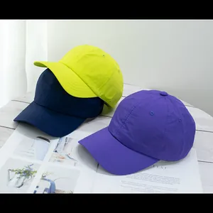 Detail view of quick-dry baseball caps in neon yellow, navy, and purple on a wood table