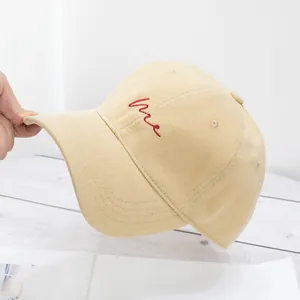 Close-up of beige corduroy baseball cap with red embroidered Me lettering detail