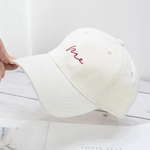 Detail of white cotton baseball cap showing red Me embroidery and curved brim