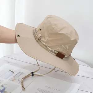 Detail of beige sun hat with mountain embroidery, metal eyelets, and adjustable chin strap
