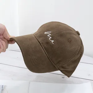 Detail of a brown cotton baseball cap showing white 'me' embroidery and twill fabric texture