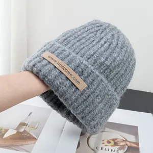 Detailed view of the chunky knit grey beanie featuring a brown leather logo patch