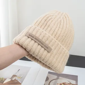Detail of beige knit beanie showing ribbed texture and woven label in a lifestyle setting