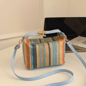 Colorful striped woven shoulder bag with light blue leather straps on a white desk