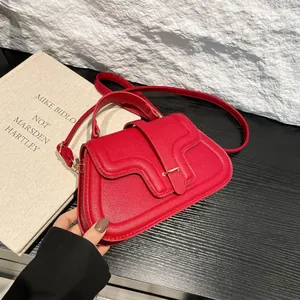 Red lychee pattern handbag with gold hardware and curved flap on wood surface