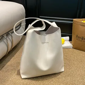 Minimalist beige leather tote bag with gold lettering in a cozy living room setting
