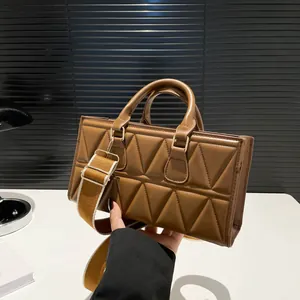 Brown triangular quilted shoulder bag with top handles and adjustable wide fabric strap