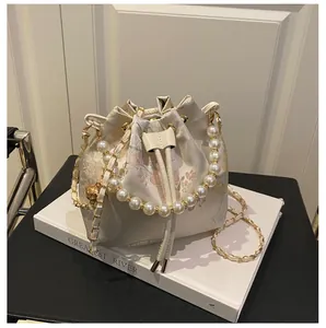Detailed close-up of a floral bucket bag with pearl handle and chain strap on books