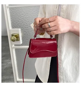 Détail d'un sac à main en cuir verni rouge foncé avec bord ondulé et bandoulière fine