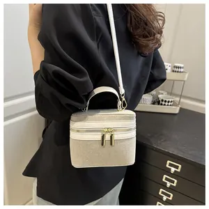 Detail of a chic cream textured box bag with gold hardware worn by a model