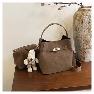 Detail der braunen Wildleder-Eimertasche mit goldenem Drehverschluss und Hund-Anhänger