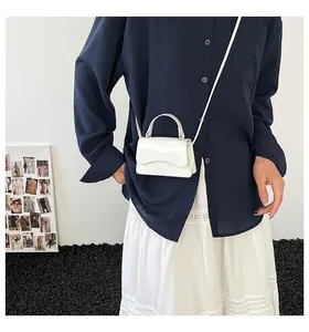 Gros plan d'un mini sac à main blanc avec rabat ondulé et finition en cuir verni brillant