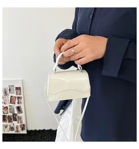 Détail d'un mini sac à main blanc brillant avec rabat ondulé porté par un mannequin