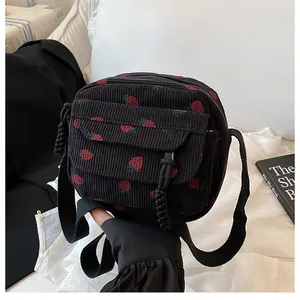 Detail view of black corduroy crossbody bag with vibrant red strawberry pattern