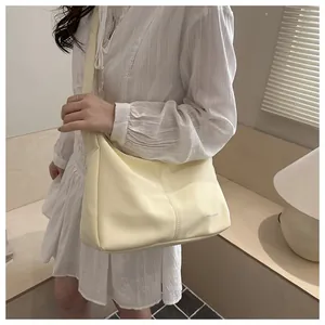 Detail view of light yellow crossbody bag with decorative stitching on a model