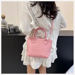 Detail of pink woven leather bucket bag featuring gold hardware and slim crossbody strap