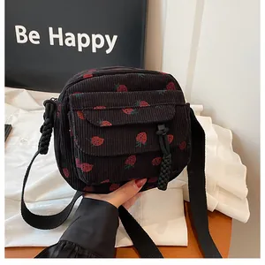 Close-up of black corduroy crossbody bag with red strawberry pattern and textured fabric
