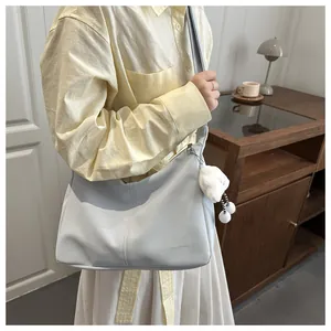 Detail of light gray crescent shoulder bag with plush pendant and brand engraving