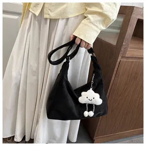 Detail of a black minimalist shoulder bag featuring a white cloud plush pendant and strap