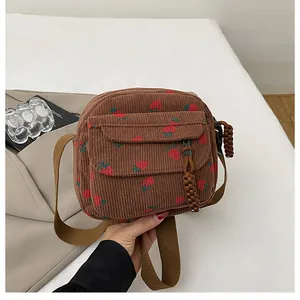 Detail of brown corduroy crossbody bag with red strawberry print and woven zipper pull